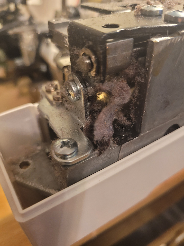 Sewing machine with lint and dust accumulation in mechanism showing the need for regular maintenance.